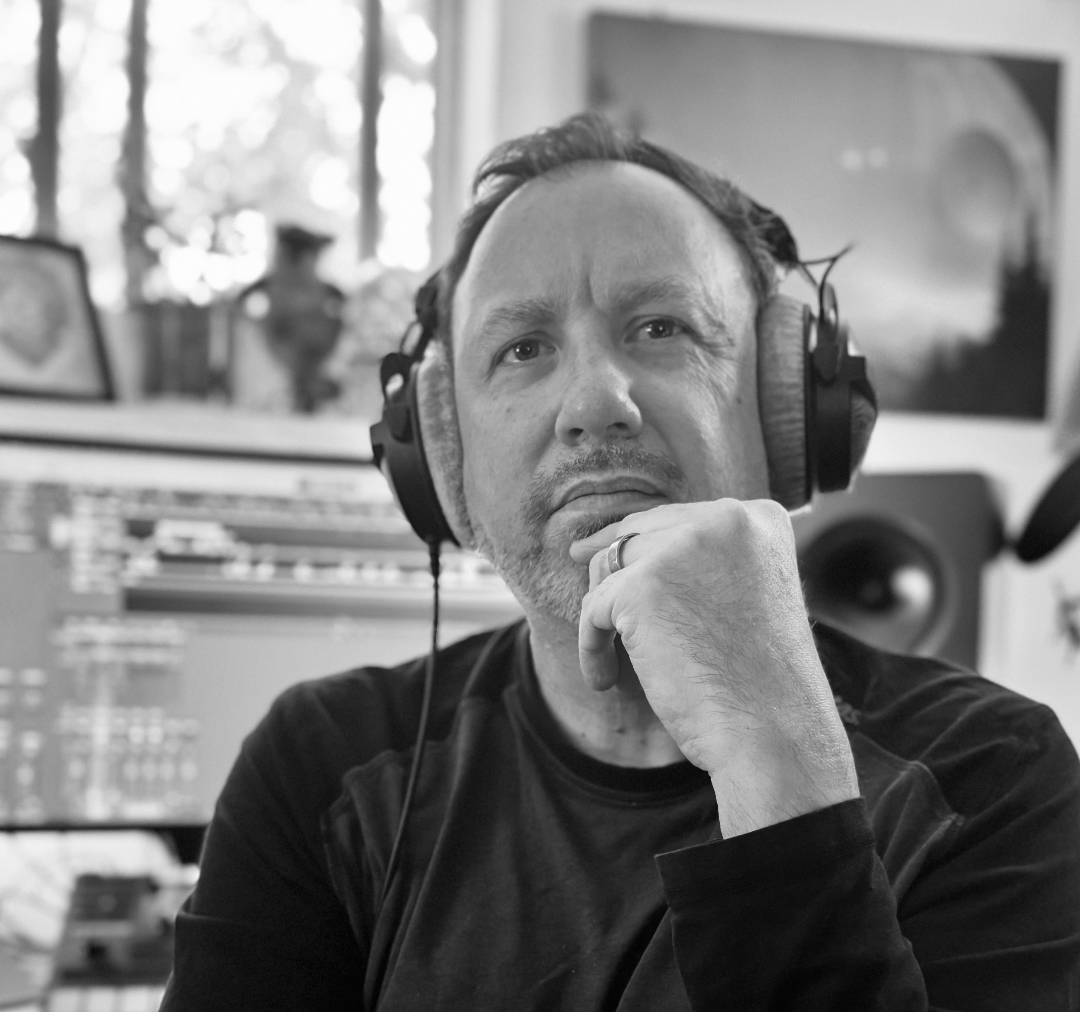 A man wearing headphones thoughtfully resting his chin on his hand in a recording studio setting.
